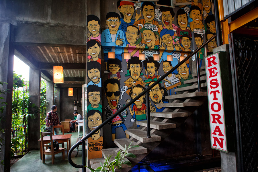  A photo of a staircase with a colorful mural of cartoon characters on the walls and a 'Restoran' sign at the top of the stairs.